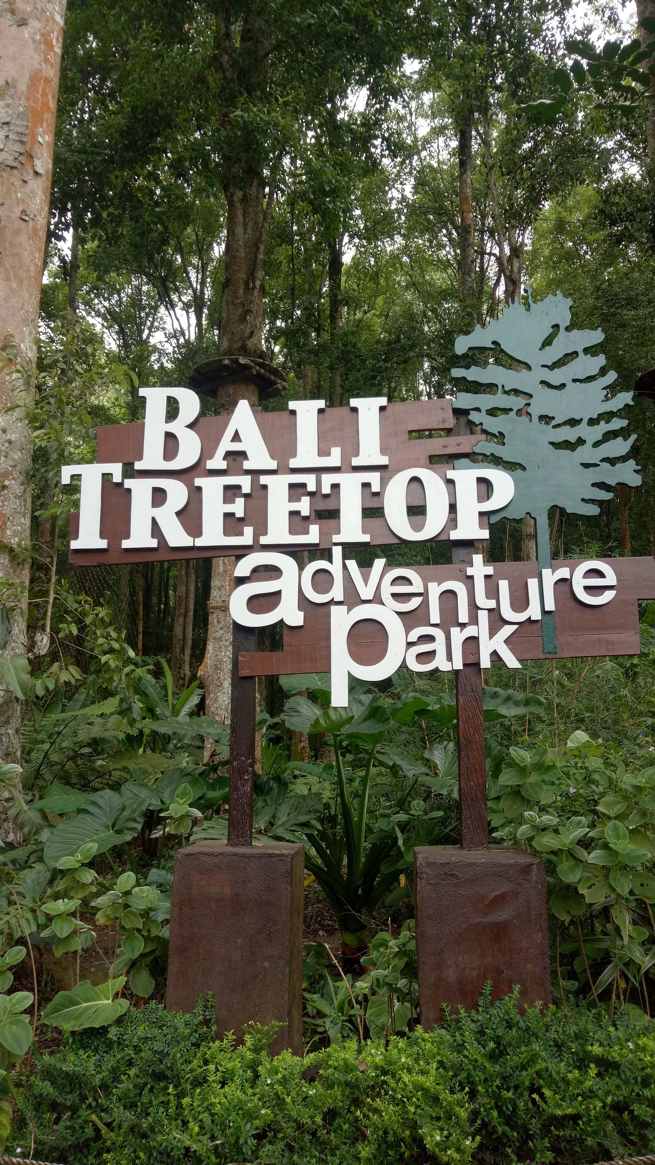 En skylt för Bali Treetop Adventure Park, omgiven av frodig grönska.