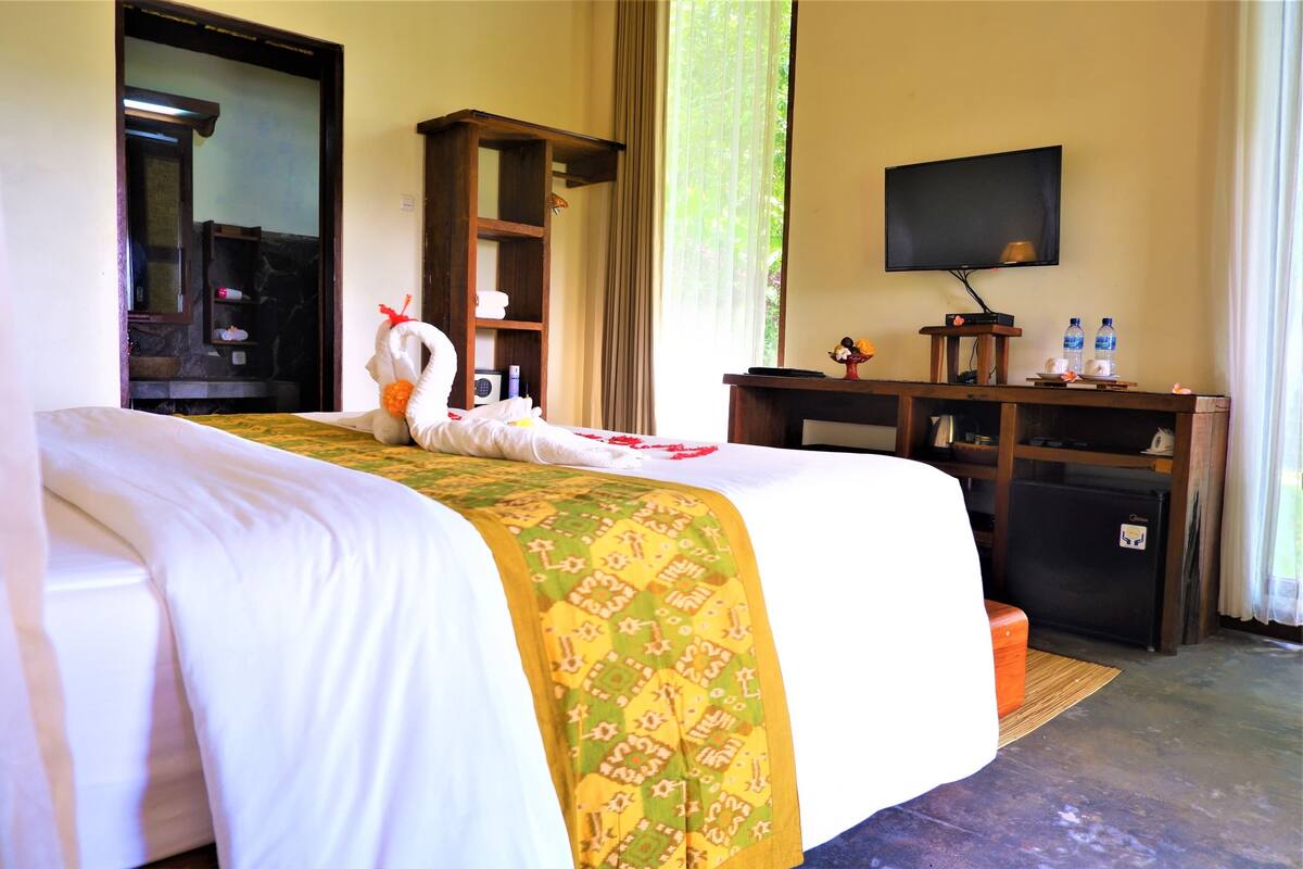 A hotel room with a bed, a television, a small refrigerator, and a desk with a mirror and shelves.