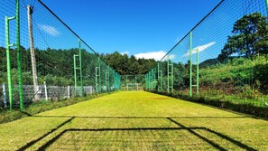 A sports field enclosed by green fencing, with a clear sky and trees in the background. - Sea and Sunset Pension (Namhae)