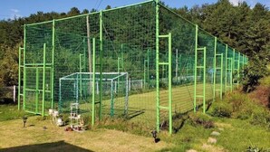 A sports field with multiple green netted areas, likely for soccer or baseball, surrounded by trees and grass. - Sea and Sunset Pension (Namhae)