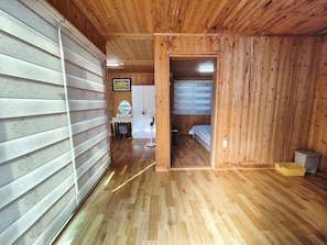 A wooden interior with a bed, a vanity with a mirror, and a small stool. - Sea and Sunset Pension (Namhae)