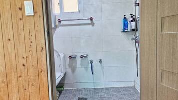 A bathroom with a wooden door, a toilet, a shower area with a hose, and a window.