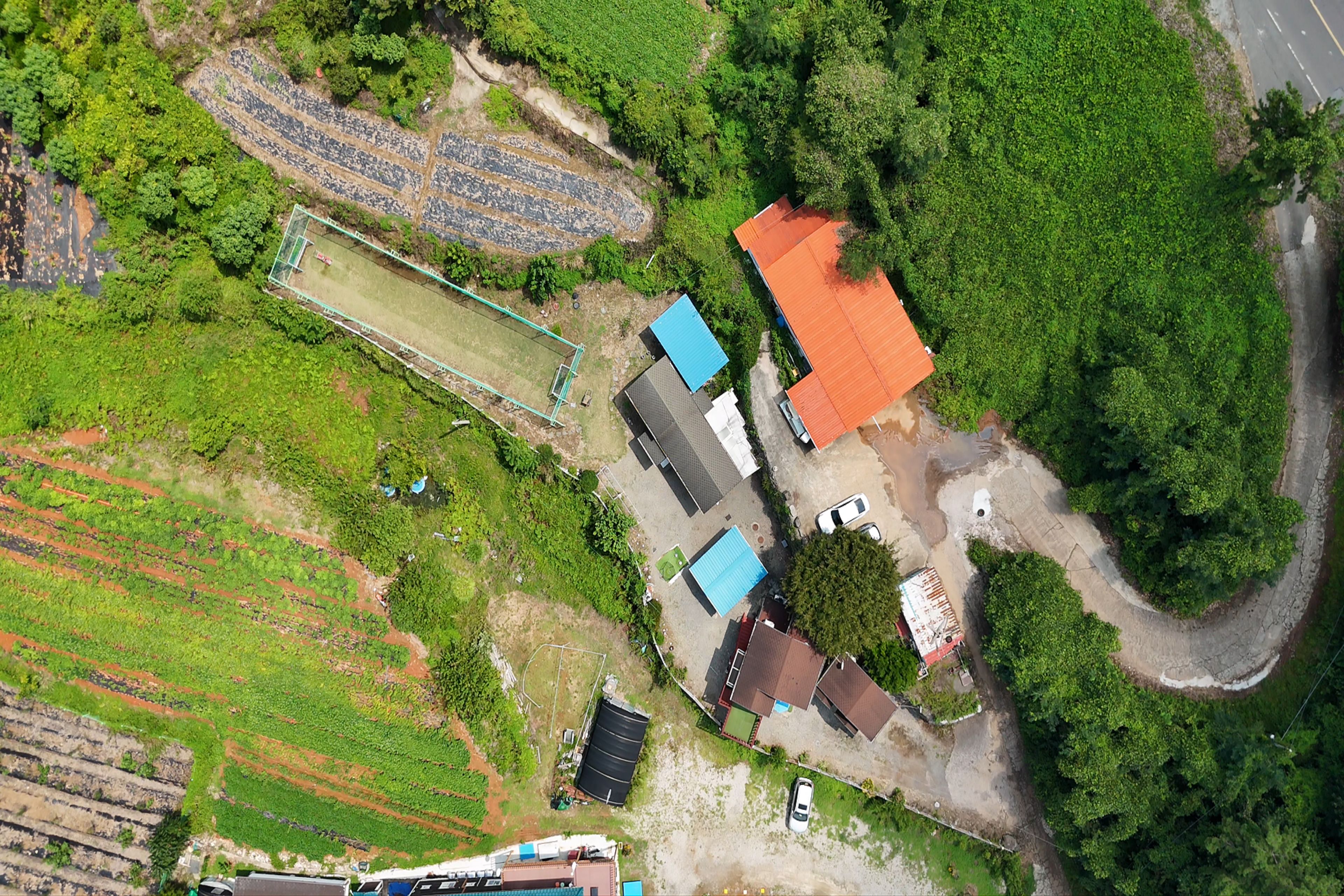 An aerial view of a residential area with a house, a fenced sports field, and surrounding greenery.