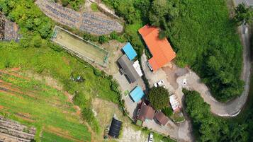 An aerial view of a residential area with a house, a fenced sports field, and surrounding greenery.