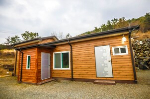 Una cabaña de madera de dos pisos con puerta principal, ventana y una puerta con panel de vidrio esmerilado.
