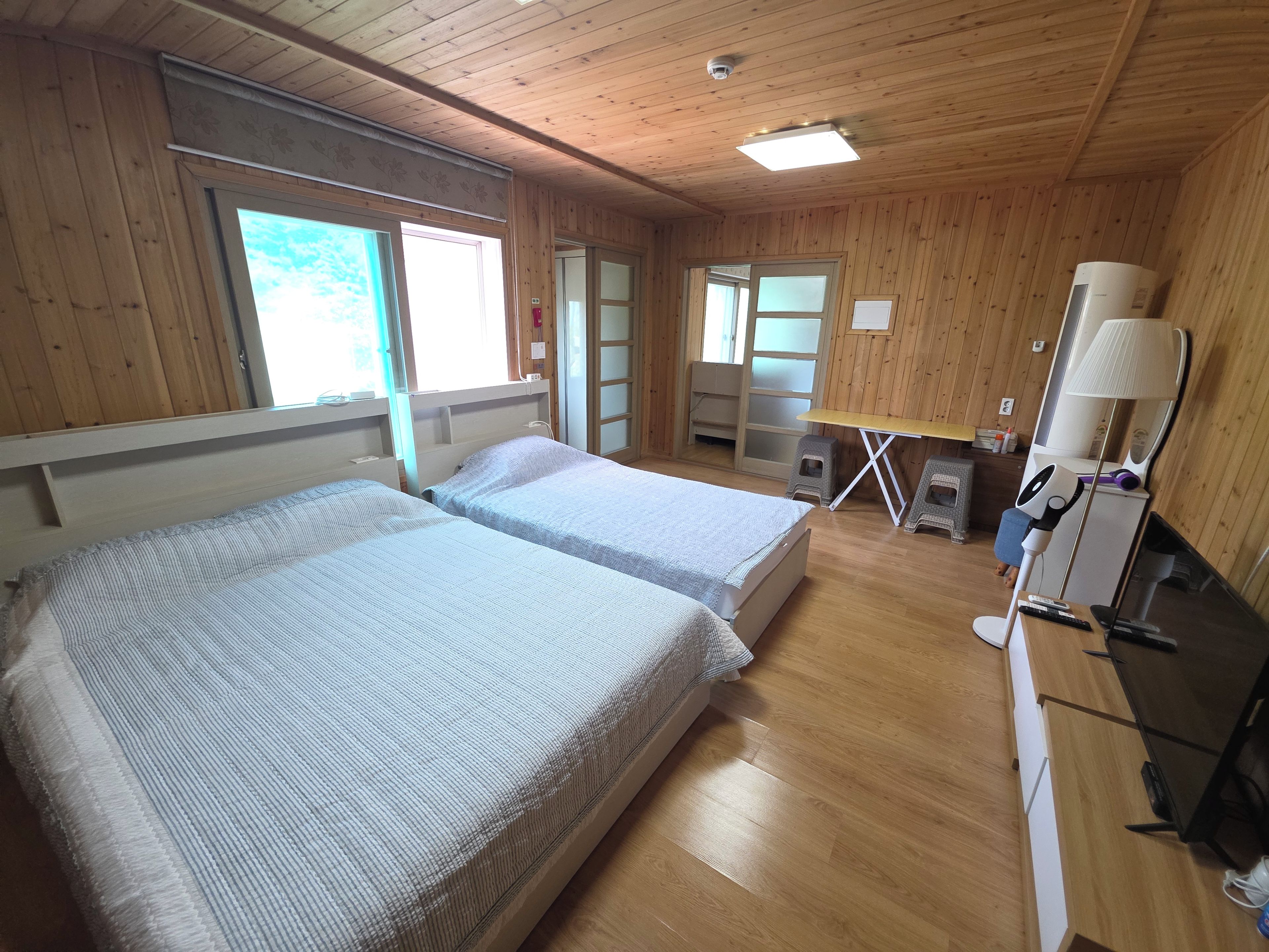 A room with wooden walls, two beds, a desk, a lamp, and a mirror.