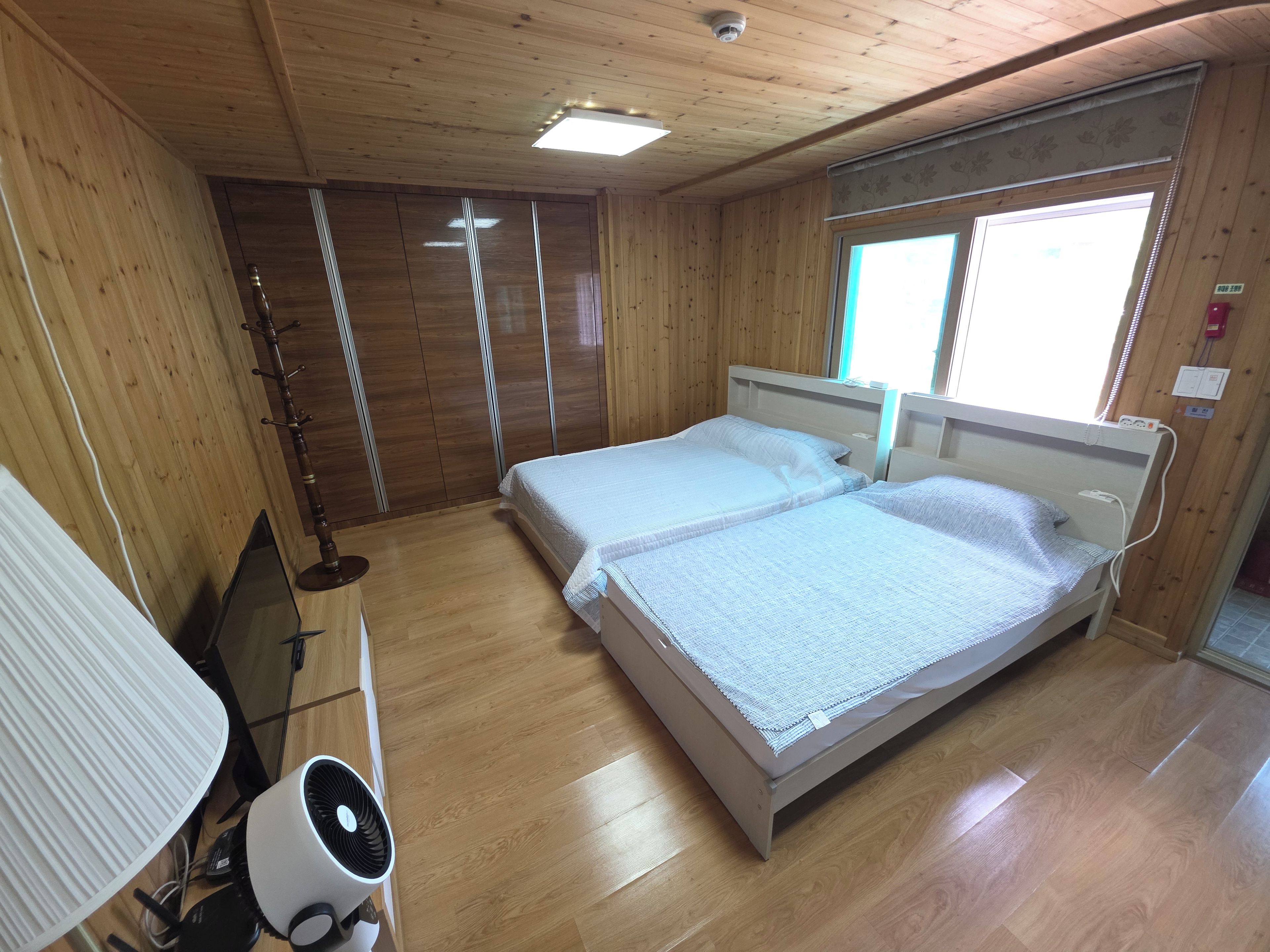 Habitación con dos camas, piso de madera, ventilador de techo y ventana con persianas.