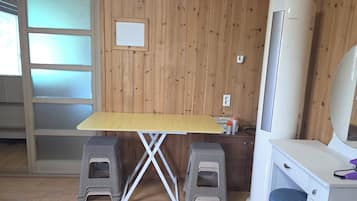 Una habitación con un revestimiento de madera, un escritorio blanco con un taburete, un aparador blanco y un equipo de aire acondicionado grande.