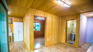 Ein geräumiges Zimmer mit Holzwänden und -böden, einem weißen Kleiderschrank, einem kleinen Badezimmer mit Waschbecken und einem Fenster mit Blick auf ein Gebäude.