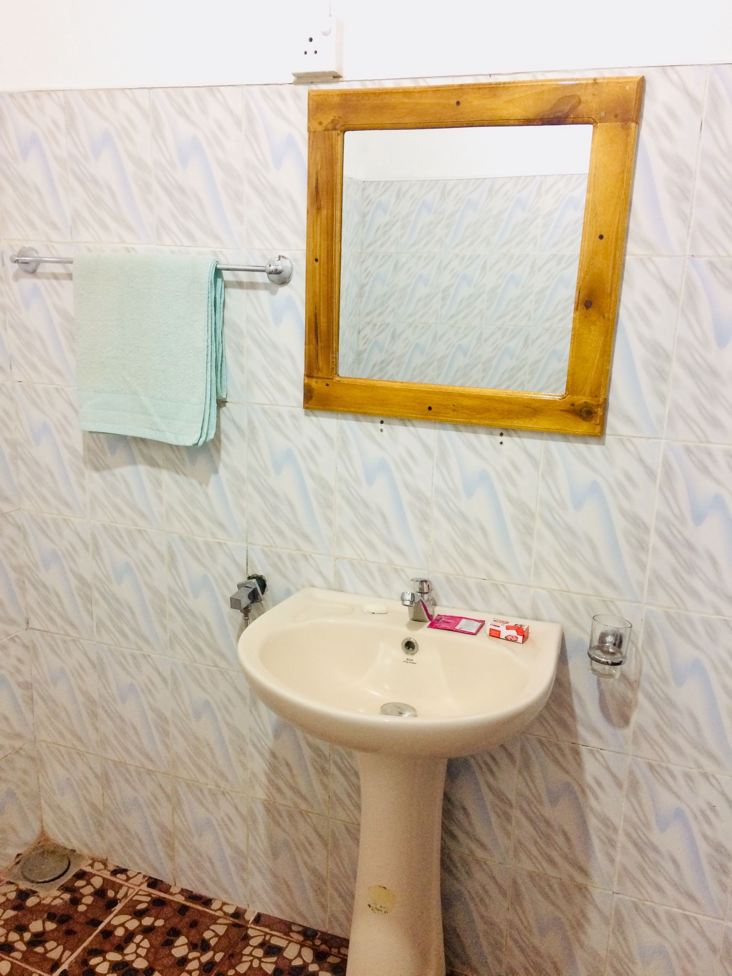 Une salle de bain avec un lavabo blanc, un miroir encadré en bois et une serviette suspendue à un porte-serviettes.