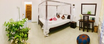 A bedroom with a four-poster bed, a bedside table with a lamp, a chair, a small table with a vase of flowers, and a large potted plant.