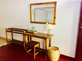 Una consola de madera con un espejo encima, un taburete pequeño, una cesta de mimbre y un jarrón con flores blancas.