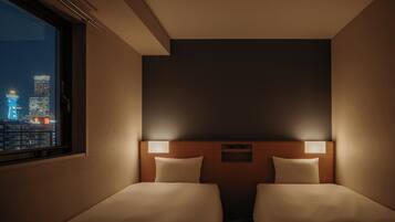 Habitación de hotel con dos camas, una mesita de noche, un ventanal con vista a la ciudad y una lámpara fijada en la pared.
