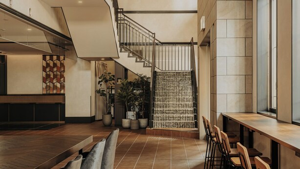 A spacious indoor area with a long wooden table and chairs, a staircase, and a view of the outside. - Nest&Rise Osaka Namba Hotel (Osaka)