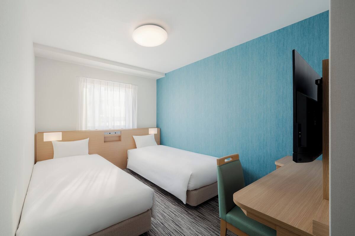 Habitación de hotel con dos camas, un escritorio, una silla, un televisor y una ventana con cortinas.
