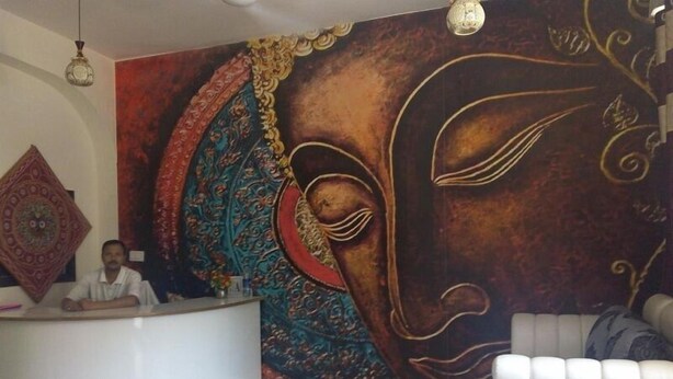 A reception area with a large mural, a round white reception desk, and a white sofa. - Jagannath Guest House (New Delhi)