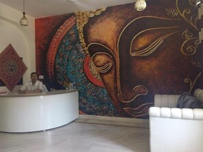 A reception area with a large mural, a round white reception desk, and a white sofa. - Jagannath Guest House (New Delhi)
