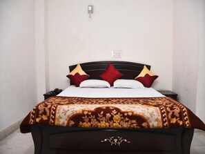 A neatly made bed with a patterned bedspread, two bedside tables, and a wall socket. - Jagannath Guest House (New Delhi)