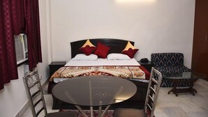 A hotel room with a bed, a round table with two chairs, a patterned sofa, and a wall-mounted light fixture. - Jagannath Guest House (New Delhi)