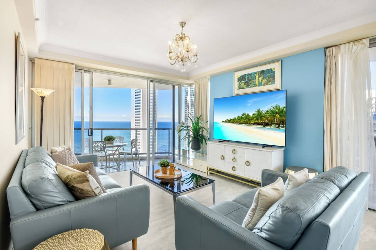 A modern living room with a balcony, a flat-screen TV, and a view of the ocean.