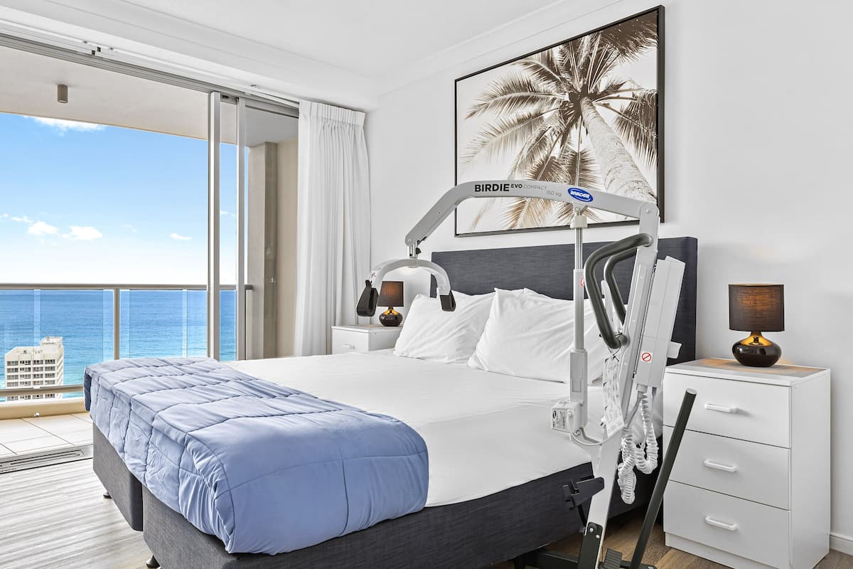 A modern hotel room with a large bed, a desk, a chair, a nightstand, and a view of the ocean.