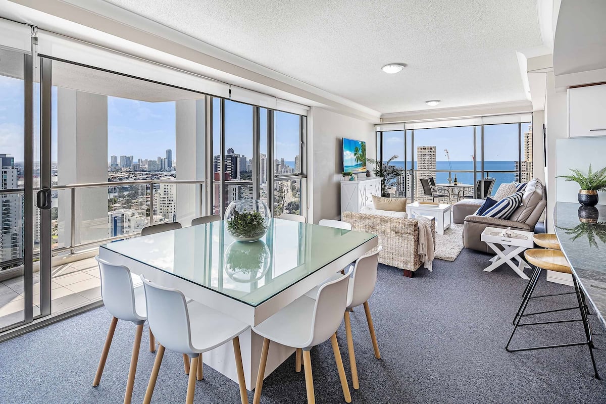 A spacious balcony with a city view, a dining area with a glass table, and a living space with a sofa and coffee table.
