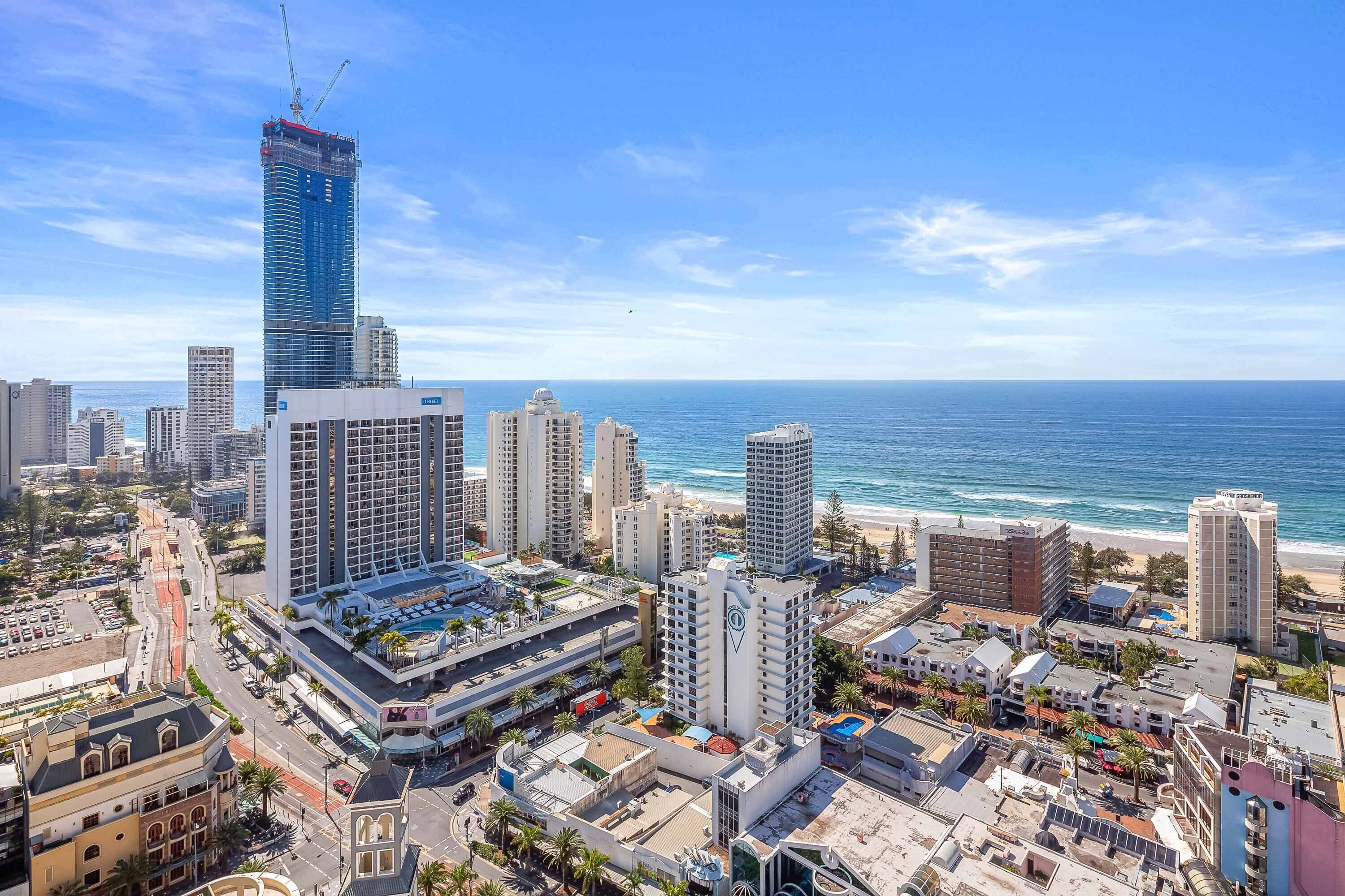 A coastal cityscape with a prominent skyscraper under construction, various mid-rise buildings, and a beach in the background.