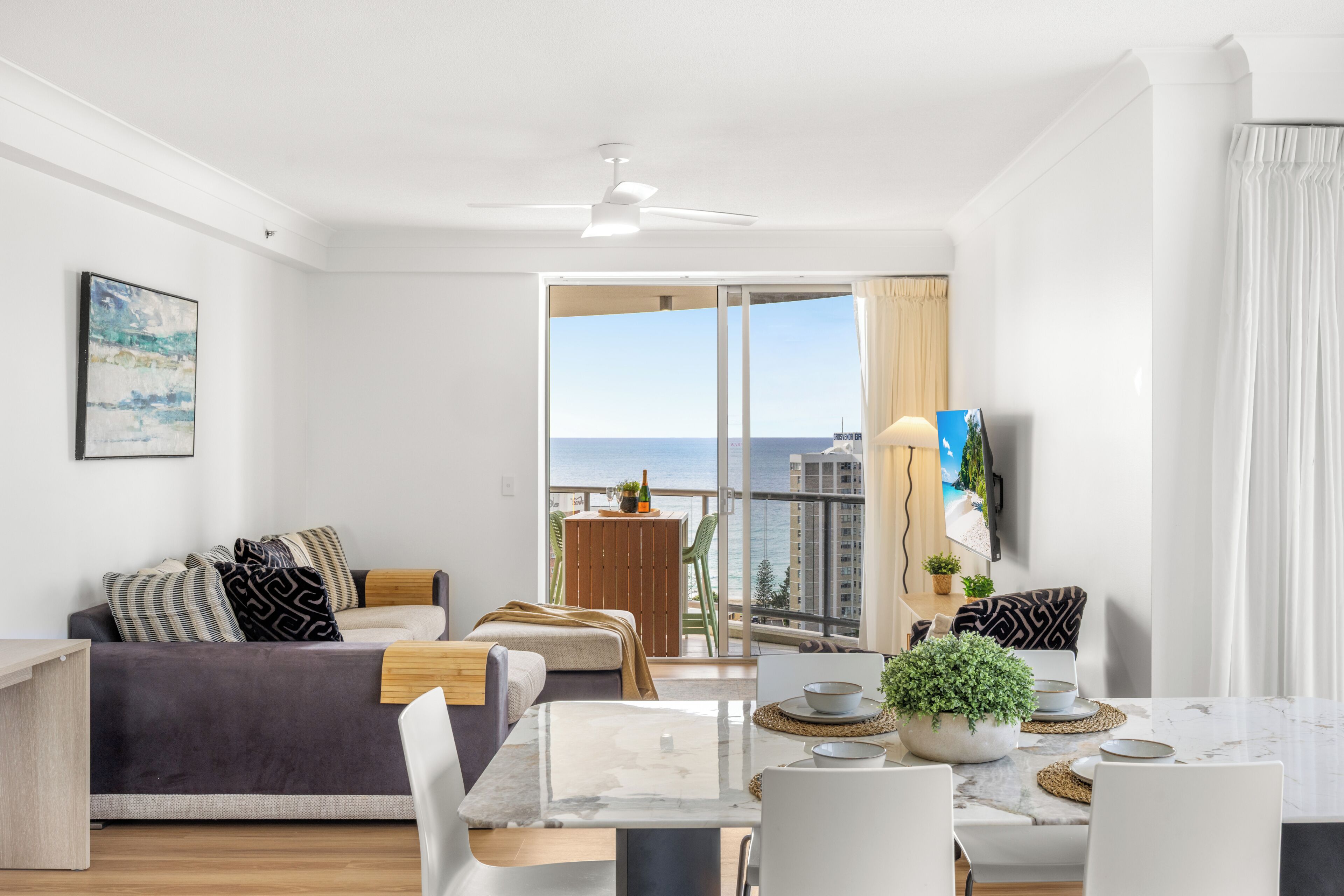 Una sala de estar moderna con sofá, mesa de comedor y balcón con vista al mar.