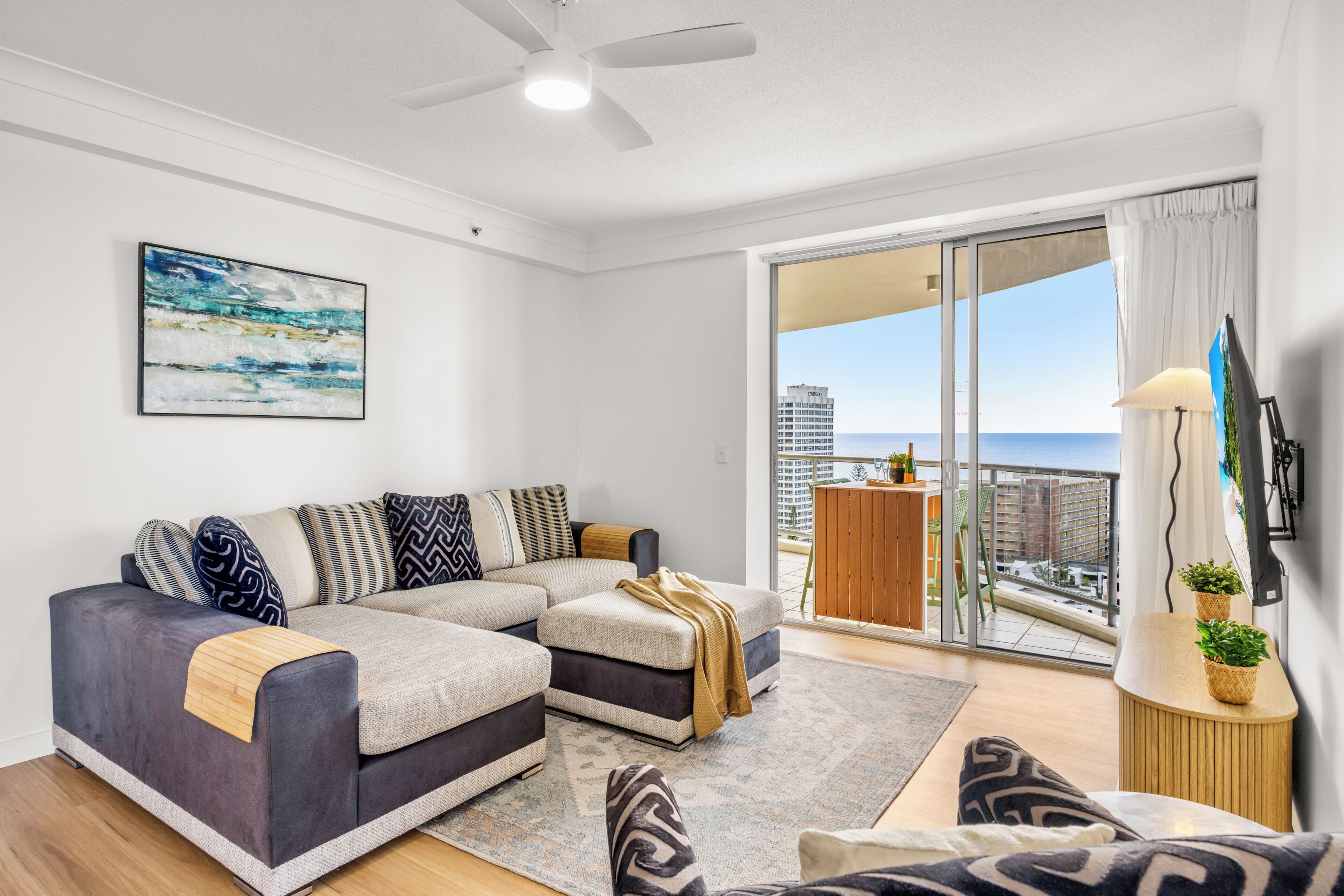 A modern living room with a sectional sofa, a coffee table, and a view of the cityscape through large sliding doors.