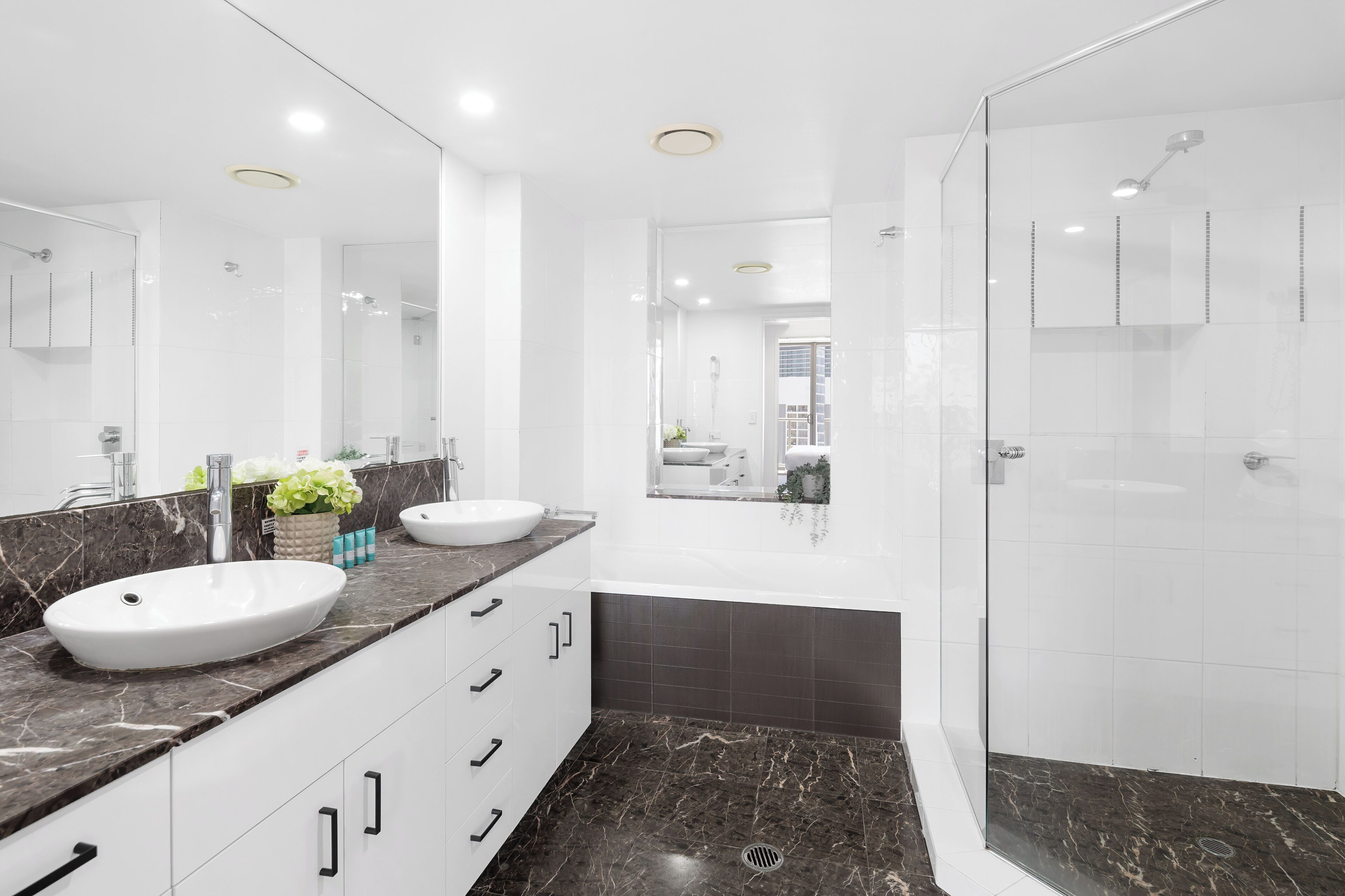 Un baño moderno con un lavamanos grande de color blanco, encimera de mármol oscuro y ducha con mampara de cristal.