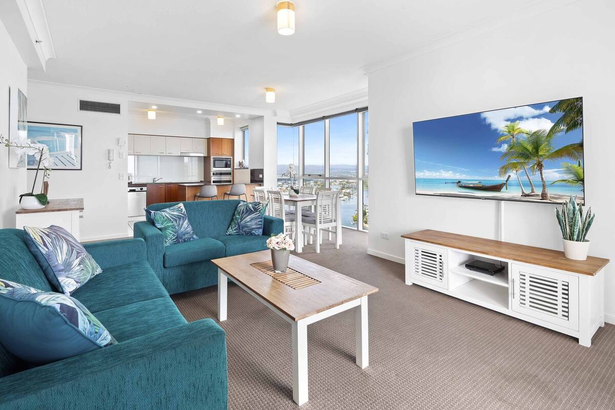 A modern living room with a sofa, coffee table, and a TV displaying a beach scene.