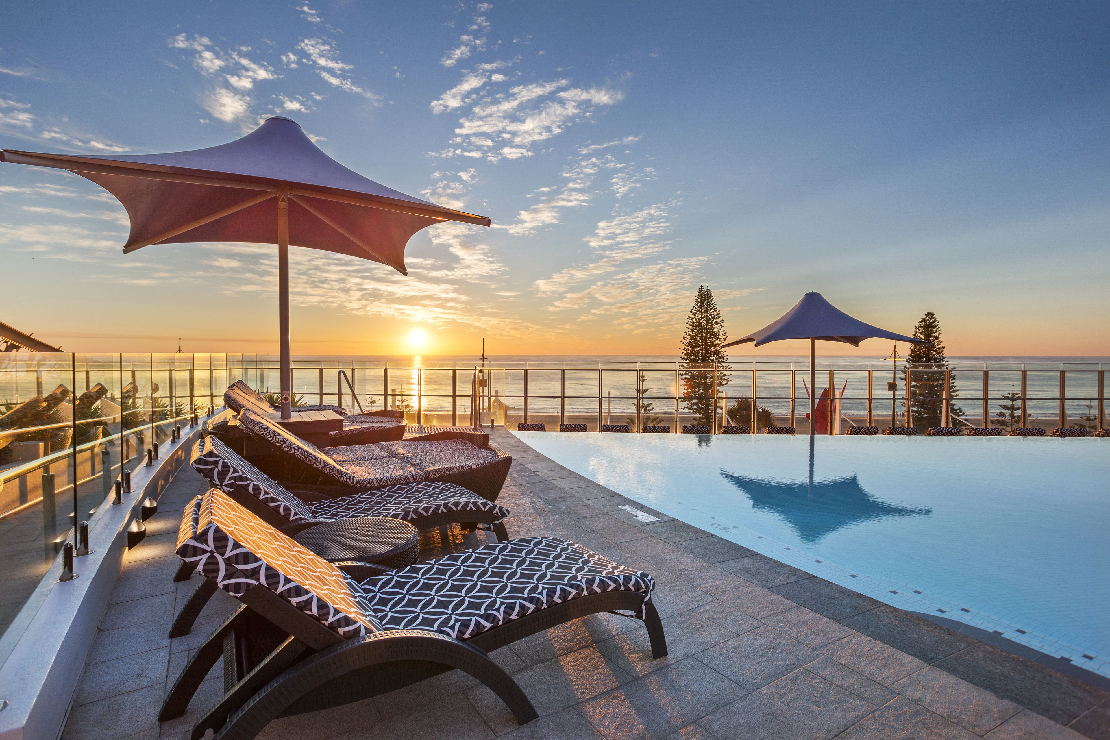 A poolside area with lounge chairs and umbrellas, overlooking a body of water at sunset.