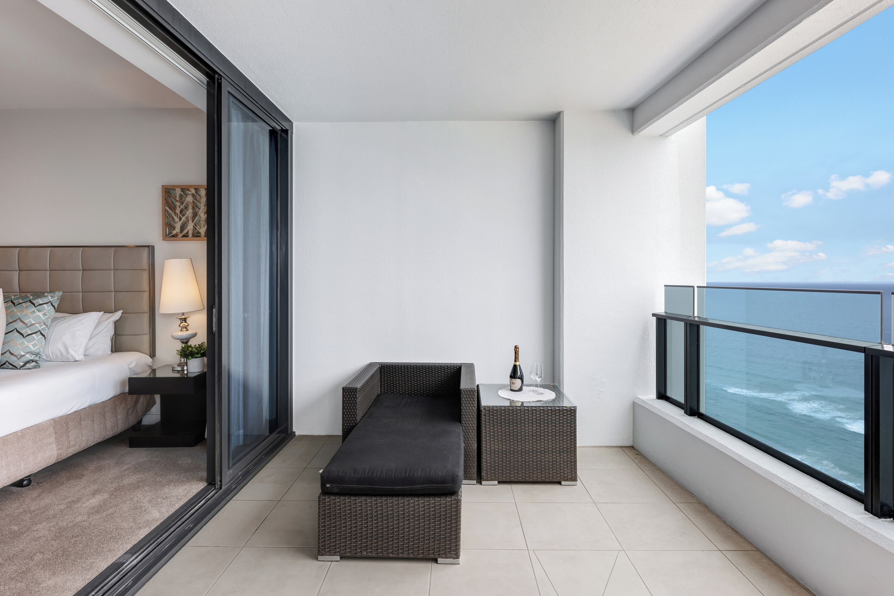A balcony with a bed, a small table with a bottle, and a chair.