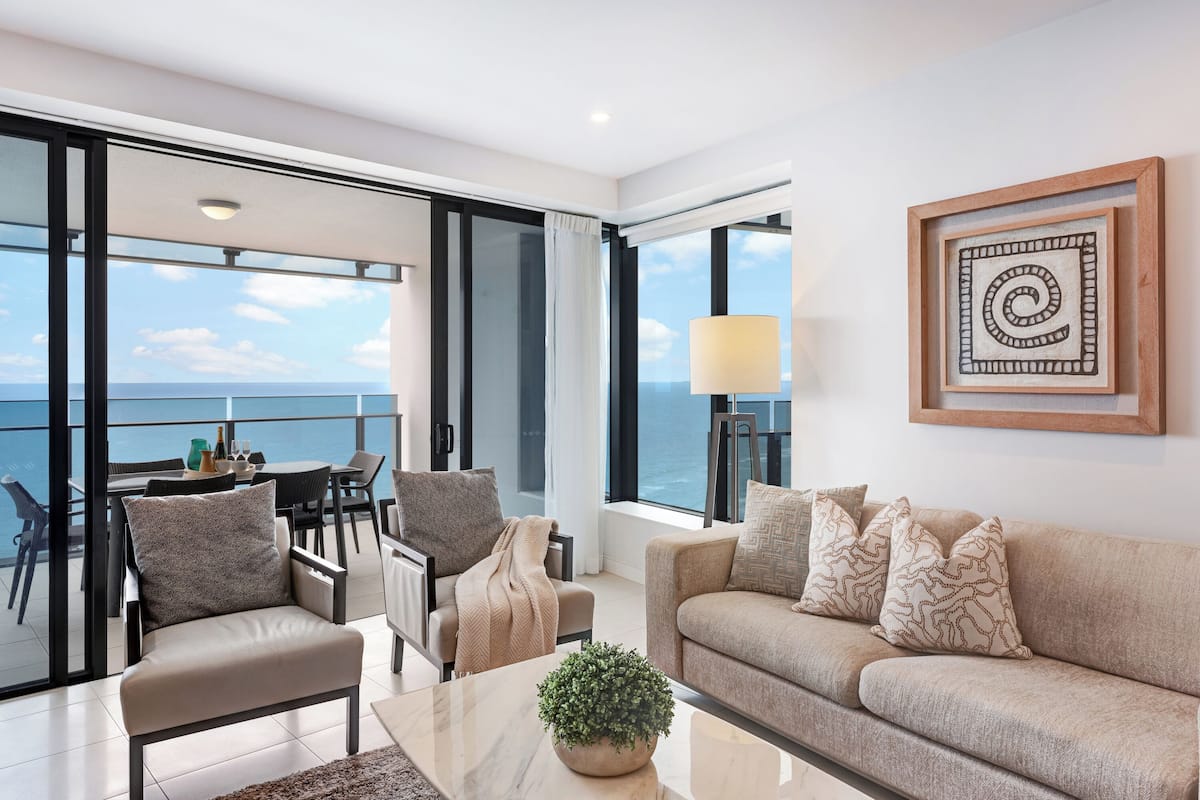 Een moderne woonkamer met een bank, fauteuils, een salontafel en uitzicht op zee.