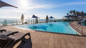 An infinity pool with lounge chairs and umbrellas, overlooking a beach and ocean. - Holiday Holiday Soul Surfers Paradise (Surfers Paradise)