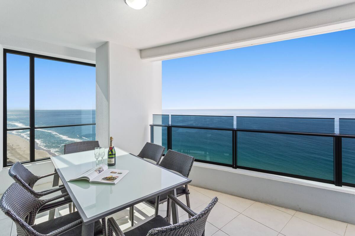 Een moderne eetruimte met een glazen tafel en rieten stoelen, met uitzicht op de oceaan.