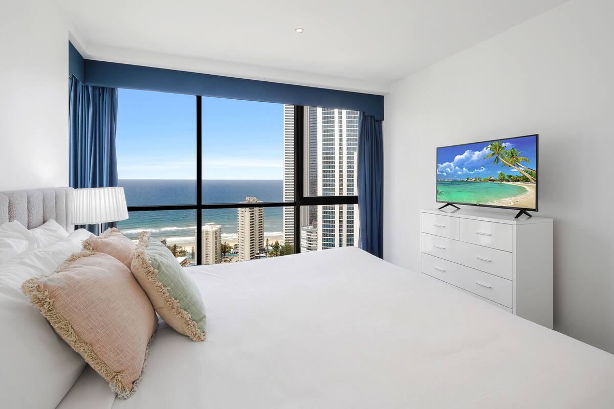 A bedroom with a large bed, a TV, and a view of the ocean.