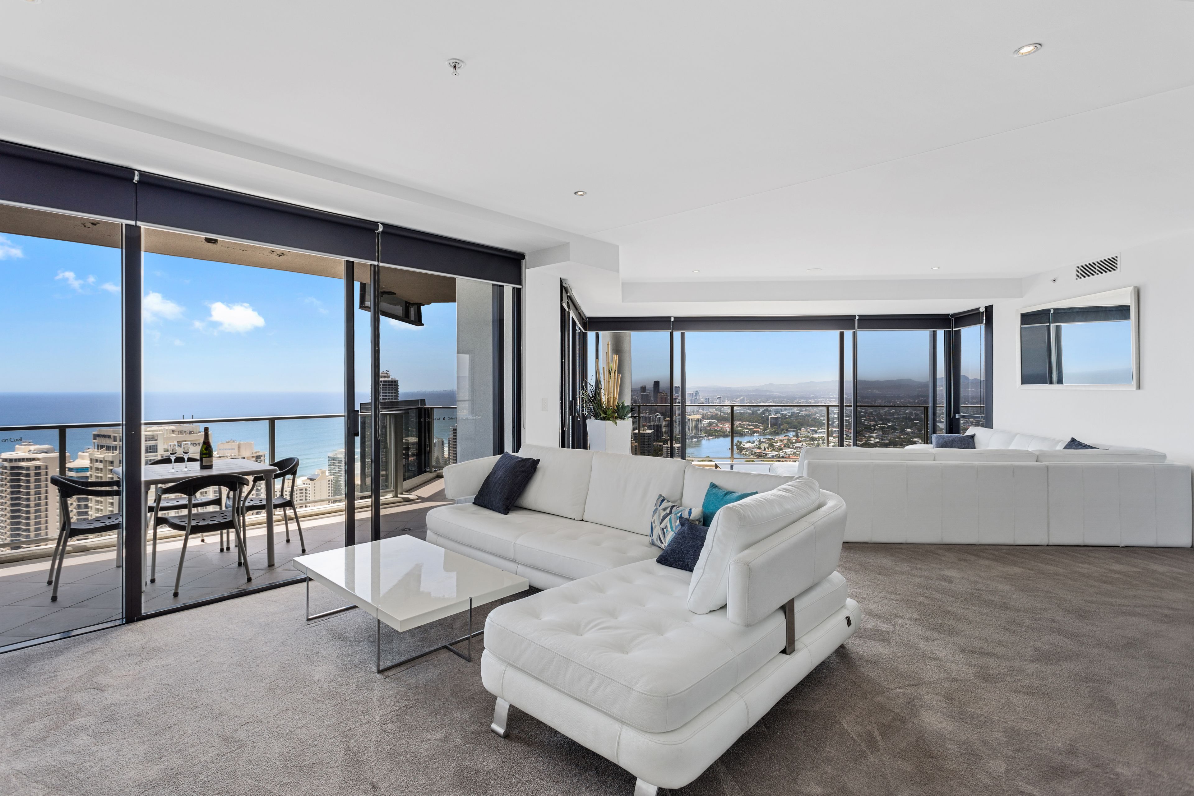A modern living room with a white sofa, a glass dining table, and a city view.