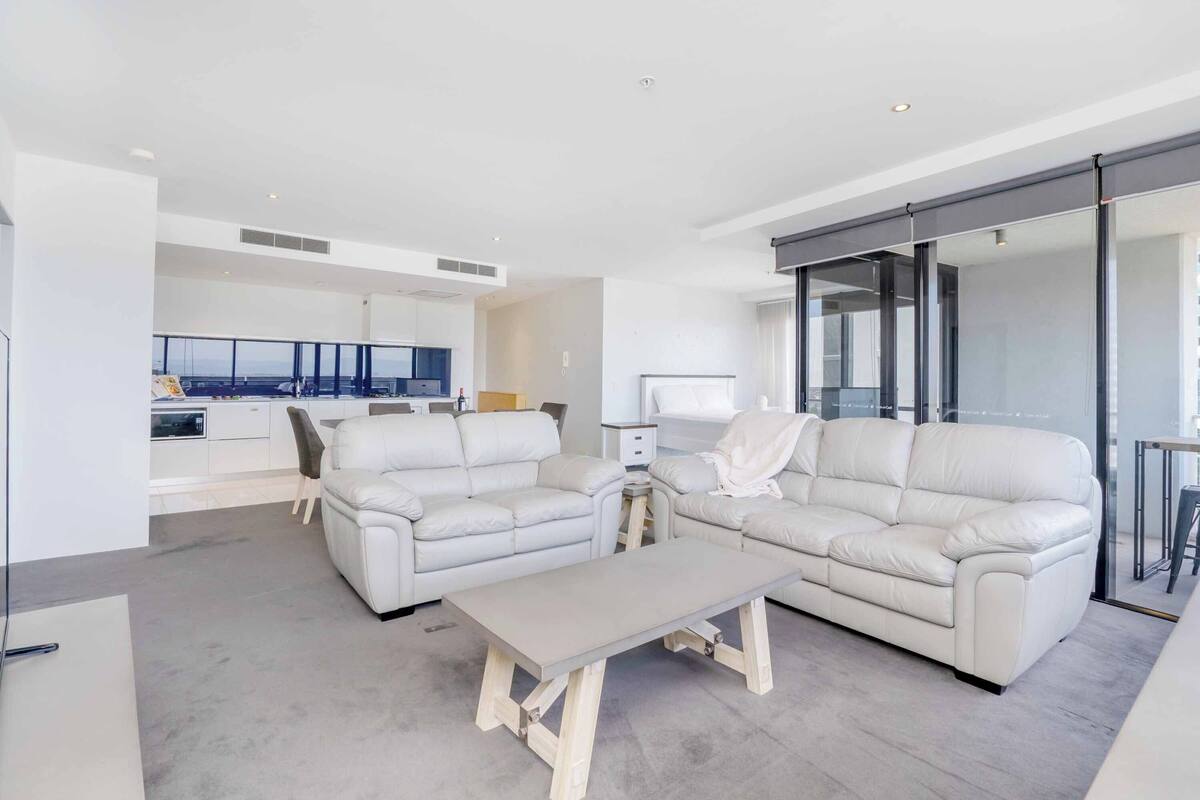 A modern living room with a sofa set, a coffee table, and a kitchen area in the background.