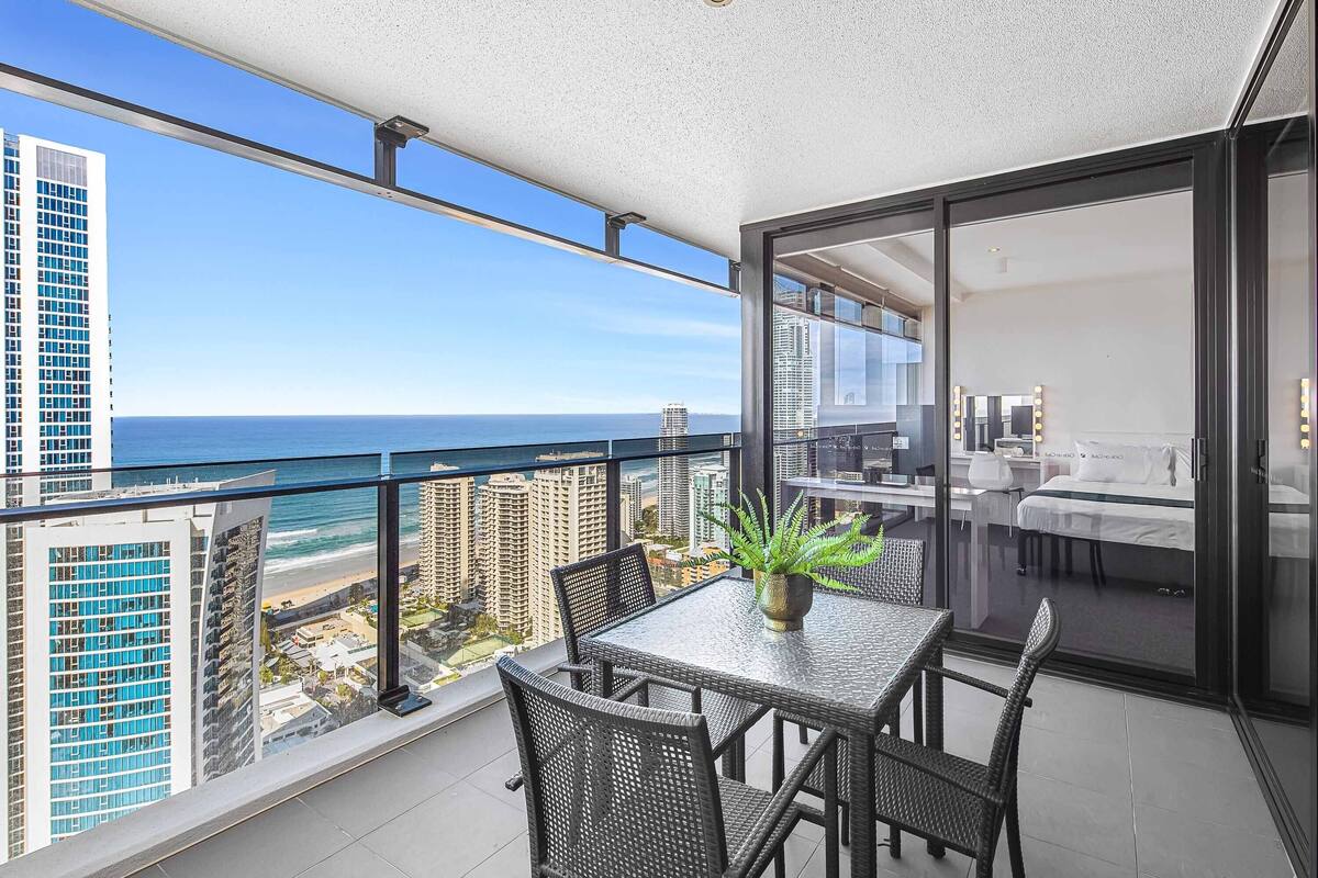 A balcony with a view of the ocean, a dining table with chairs, and a potted plant.