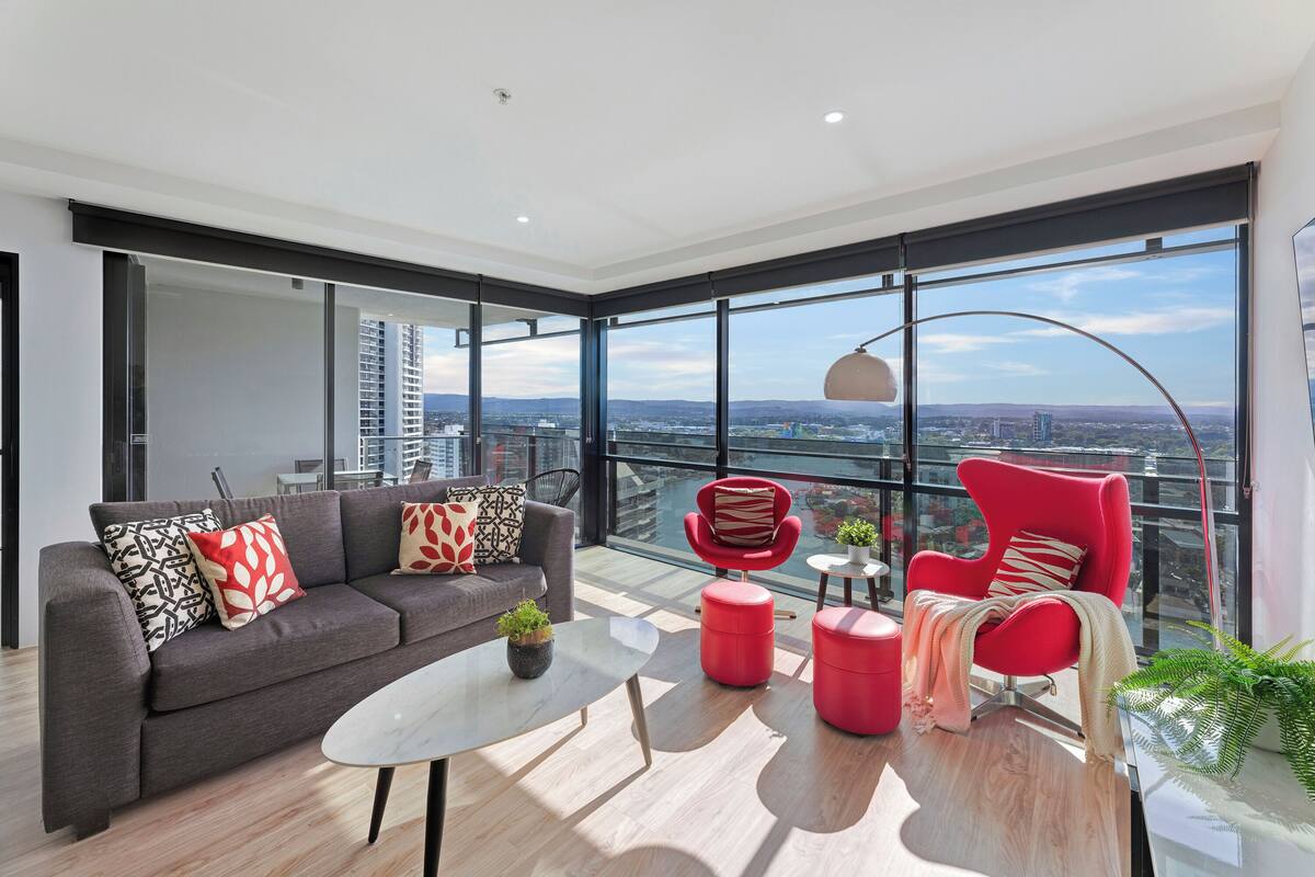 A modern living room with a grey sofa, red armchair, and glass coffee table.