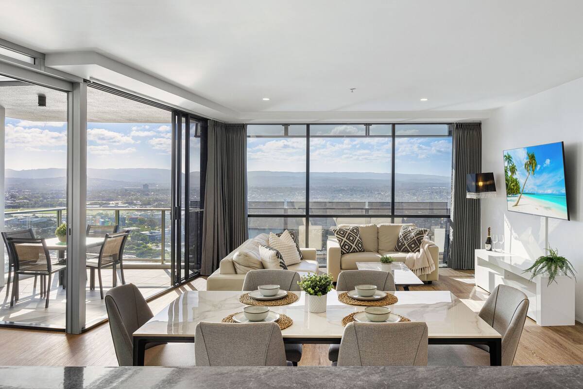 A modern living room with a large dining table, comfortable seating, and a city view through expansive windows.