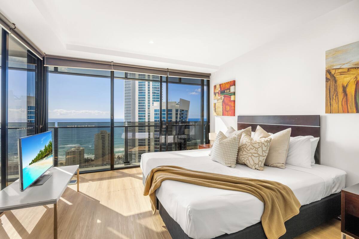 A modern hotel room with a large bed, a TV, and a balcony with a city view.