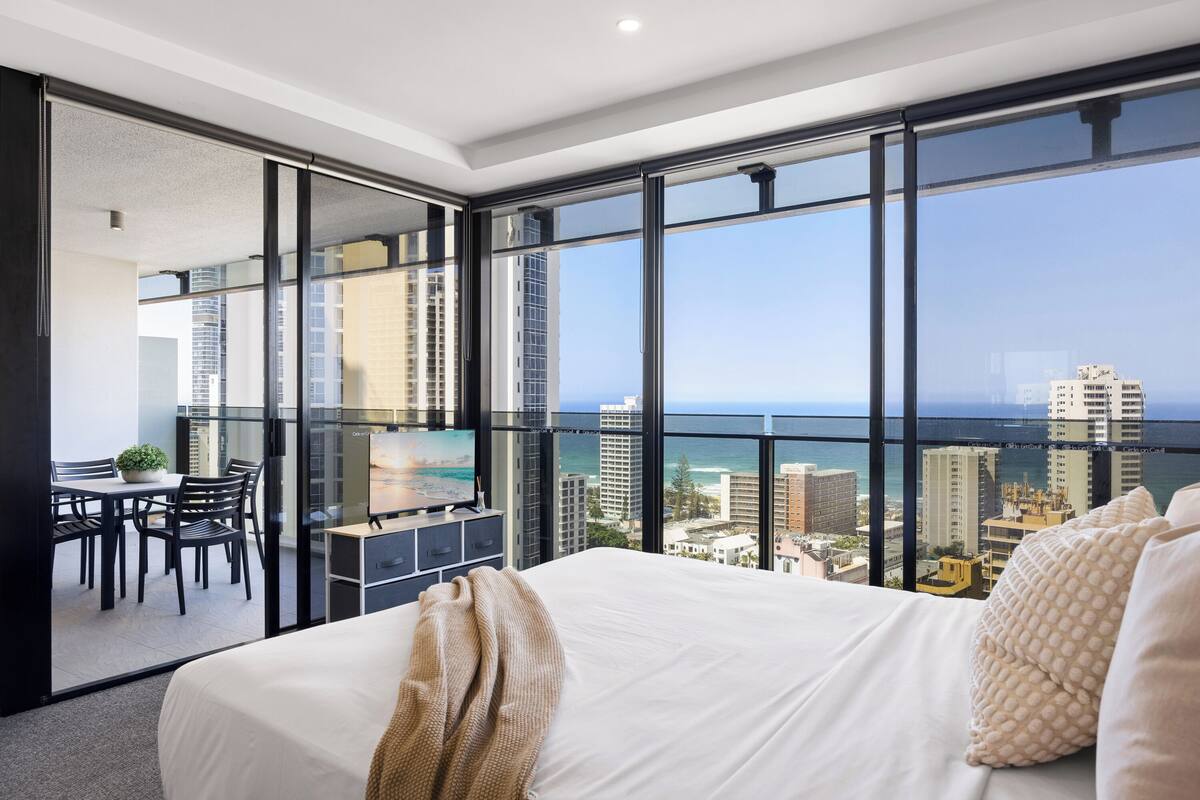 A hotel room with a large bed, a dining area with a table and chairs, and a balcony with a city view.