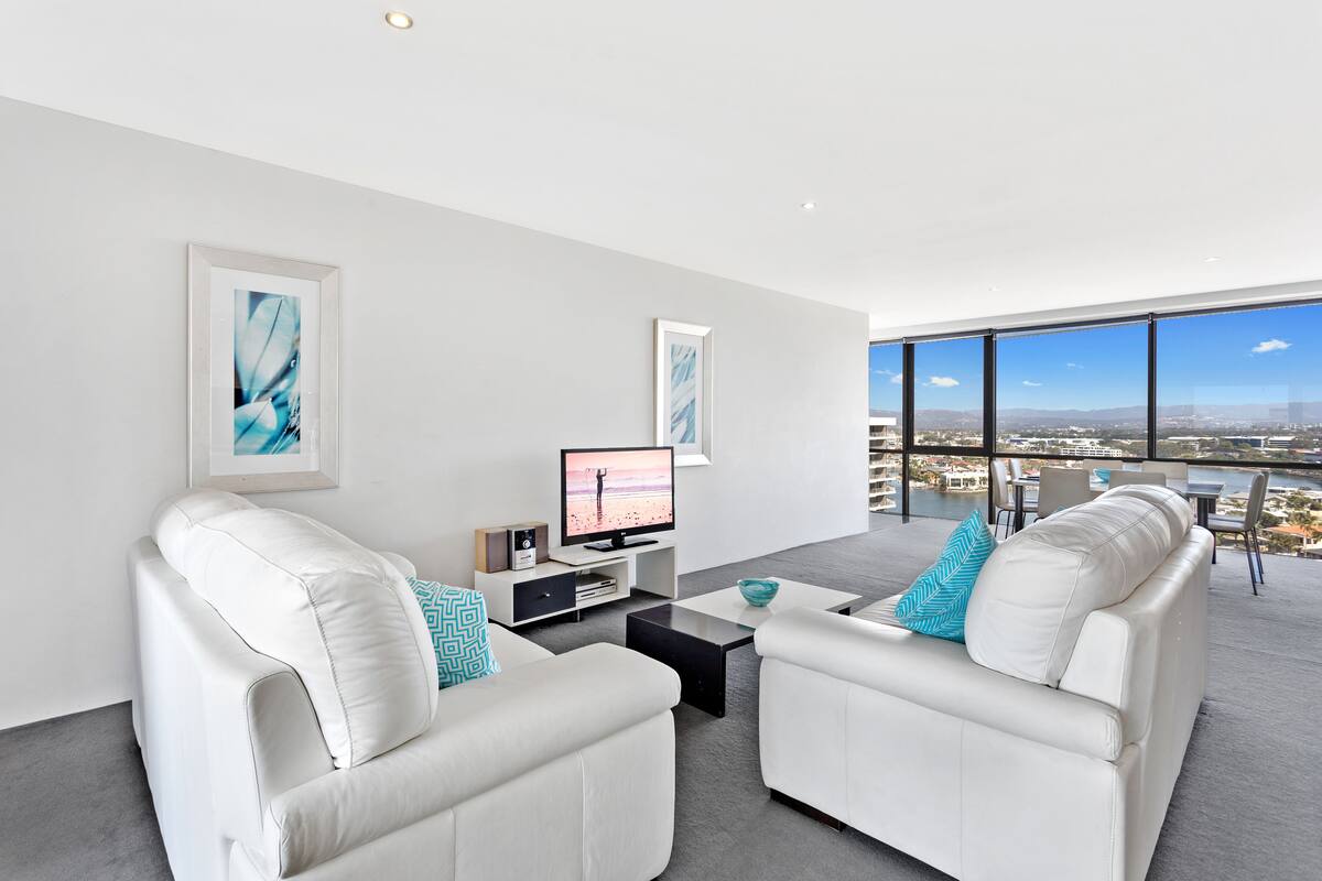 A modern living room with white sofas, a flat-screen TV, and artwork on the walls.