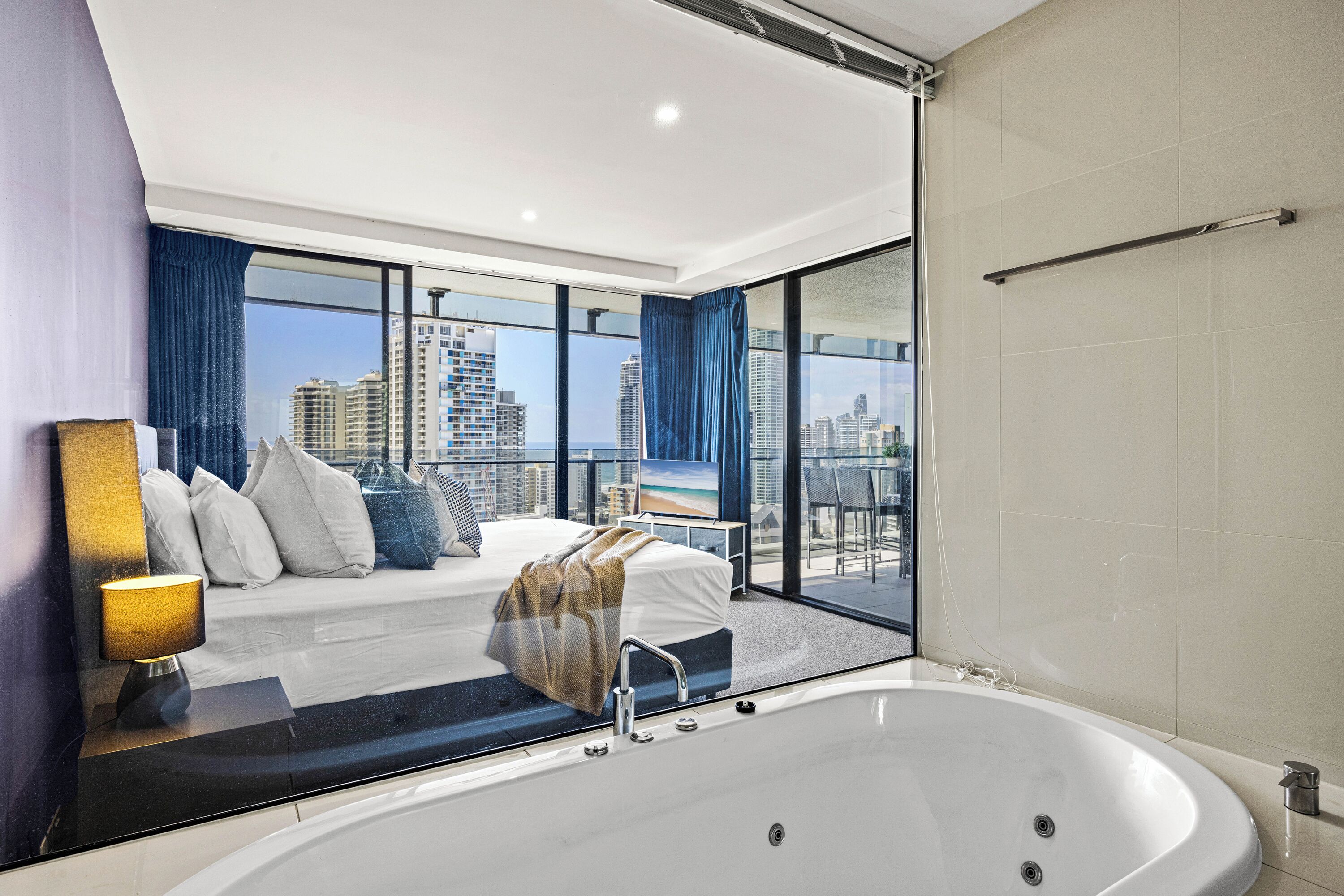 Una habitación de hotel moderna con una bañera grande, una cama con vistas a la ciudad y un balcón con panorama urbano.