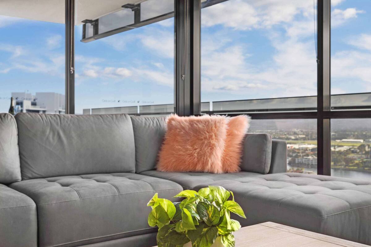 A modern living room with a grey sofa, a fluffy orange pillow, and a green plant on a wooden table.