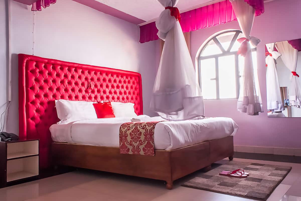 A bedroom with a red tufted headboard, white bedding, and a canopy bed.