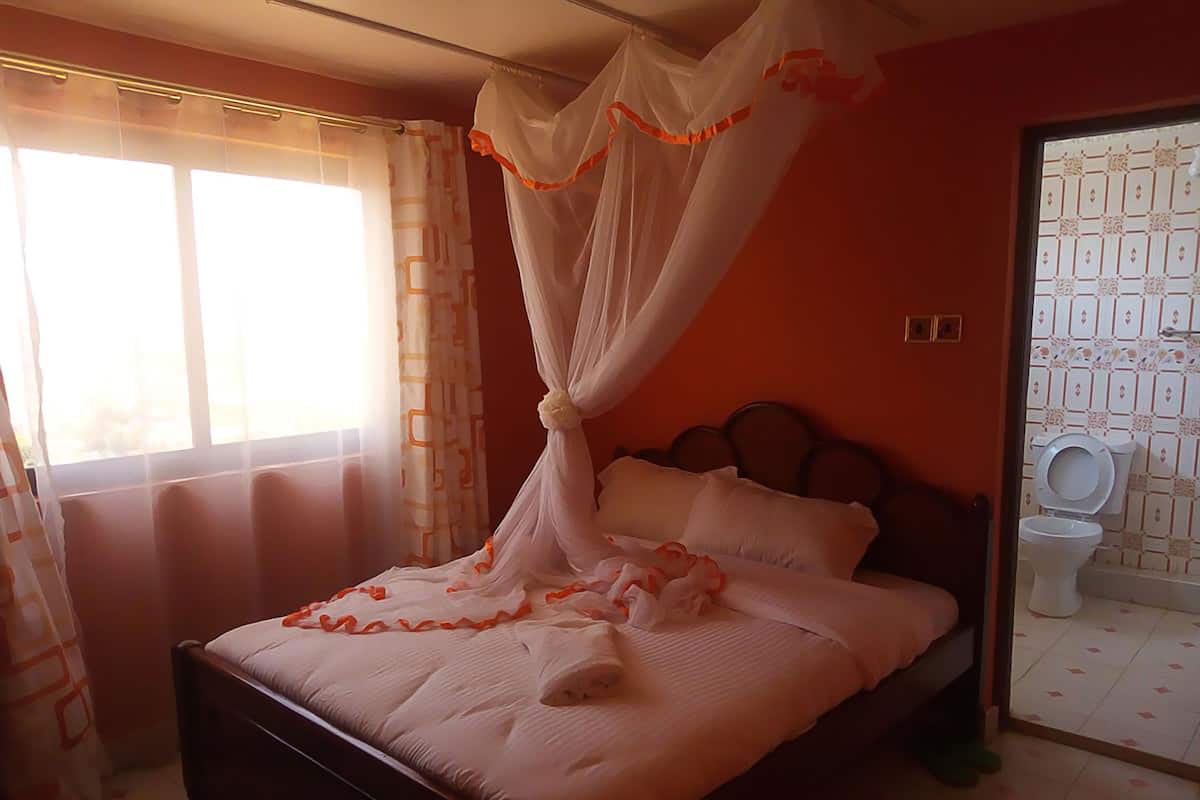 A bedroom with a bed, a window with curtains, a toilet, and a shower area.