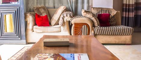 A living room with a sofa and armchair, a wooden coffee table with a magazine, and a patterned rug.